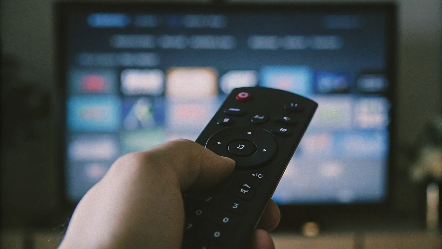 Hand holding a TV remote while browsing an IPTV interface